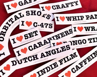 Puede incluir: Una colección de pegatinas rectangulares blancas con texto negro y un corazón rojo. Las pegatinas dicen "I Gaff Tape", "I Crafty", "I C-47s", "I Set", "I Dutch Angles", y más. Las pegatinas están sobre una superficie roja.