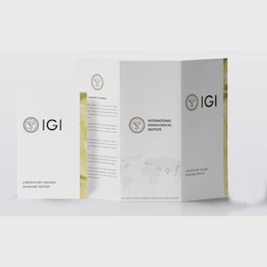 Peut inclure: Brochure blanche pliée en trois avec le logo IGI et du texte. La brochure est ouverte, affichant "International Gemological Institute" et "Laboratory Grown Diamond Report". Un léger dégradé doré est en arrière-plan.