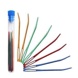 May include: A set of eight colorful plastic needles in a clear plastic tube with a blue lid. The needles are arranged in a fan shape and are all different colors: orange, yellow, green, red, and blue.