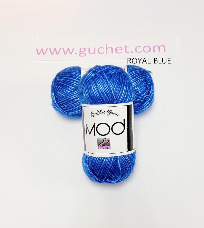 May include: Three skeins of royal blue yarn arranged in a cluster. Each skein features a white paper label with the text Guchet Yarns MOD and a logo. The text www.guchet.com and the words ROYAL BLUE are printed above the yarn on the background.