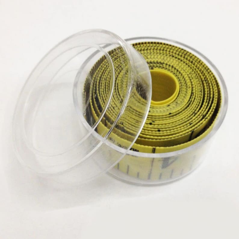 May include: A yellow measuring tape with black markings is rolled up inside a clear plastic case with a lid.