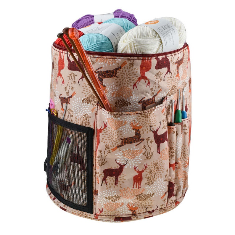 Puede incluir: Una bolsa de almacenamiento de hilo beige con un dise&ntilde;o de estampado de ciervos. La bolsa tiene un cierre de cremallera, un bolsillo de malla y varios bolsillos para guardar agujas de tejer y otros accesorios. La bolsa est&aacute; llena de ovillos de hilo de varios colores.