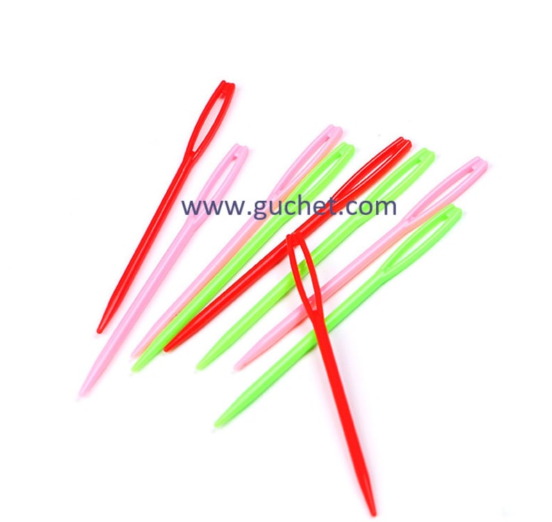 May include: A set of plastic needles in red, pink and green colours. The needles are used for threading yarn through fabric. The needles are arranged in a criss-cross pattern. The text "www.guchet.com" is visible in the image.
