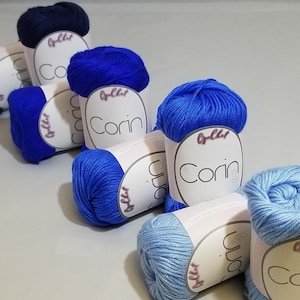 May include: Six skeins of yarn in various shades of blue. The yarn is labeled "Corin" and "O'lchi" in pink lettering.