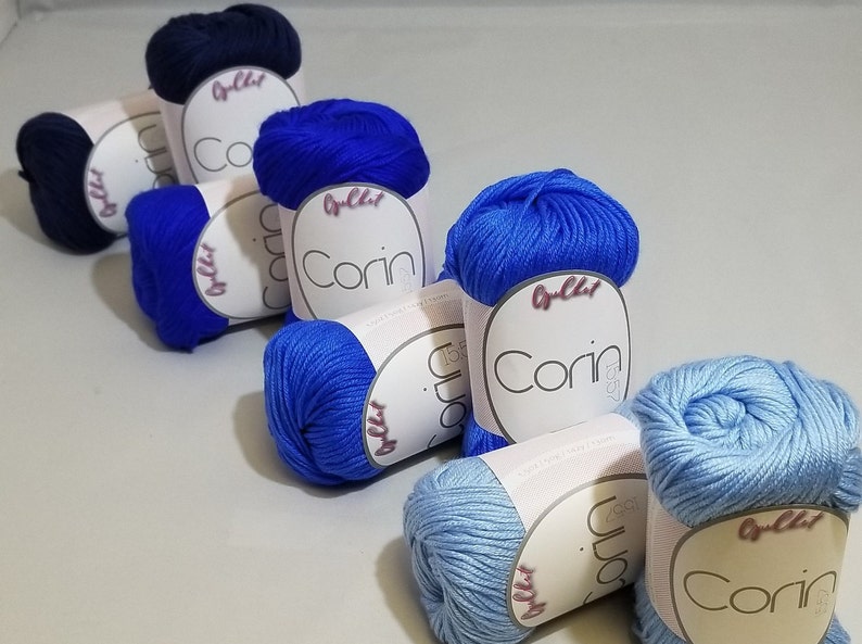 May include: Six skeins of yarn in various shades of blue. The yarn is labeled "Corin" and "O'lchi" in pink lettering.