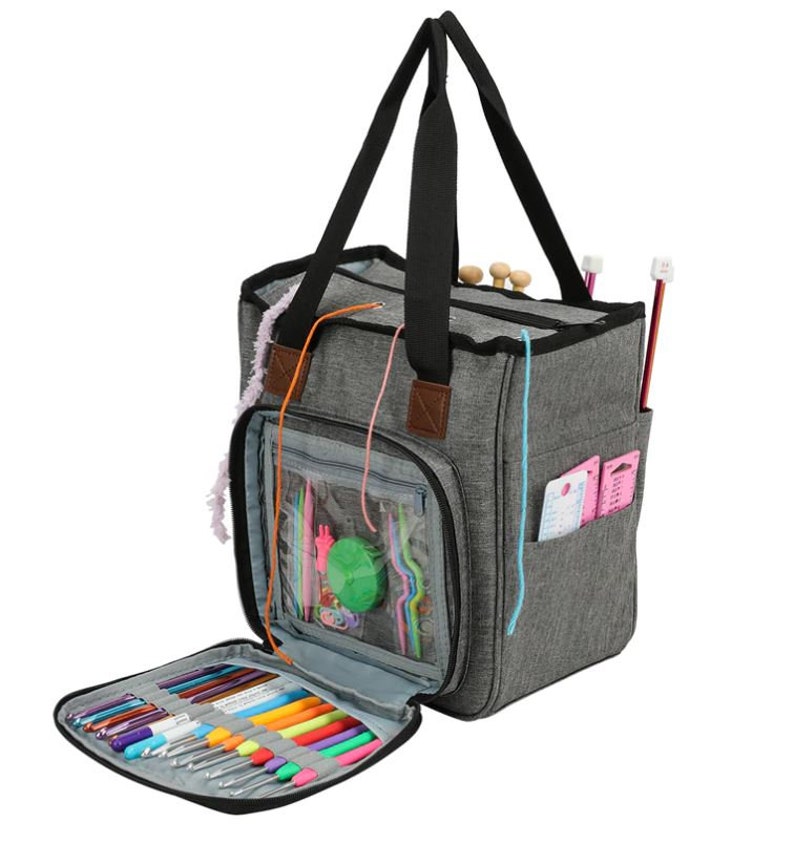 May include: A gray canvas tote bag with multiple pockets and compartments for storing knitting needles, yarn, and other craft supplies. The bag has a zippered closure and a top handle.