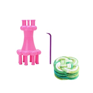 May include: A pink knitting loom with a hook and a stack of green and white knitted coasters. The loom has a flower-like base and a series of pegs for yarn. The hook is purple. The coasters are in a knot design.
