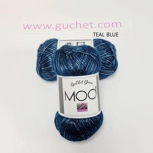 May include: Three skeins of teal blue yarn with a metallic sheen. The central label features the text Guchet Yarns MOD and a logo. The background includes the text www.guchet.com and the color name TEAL BLUE. The yarn has a twisted texture.