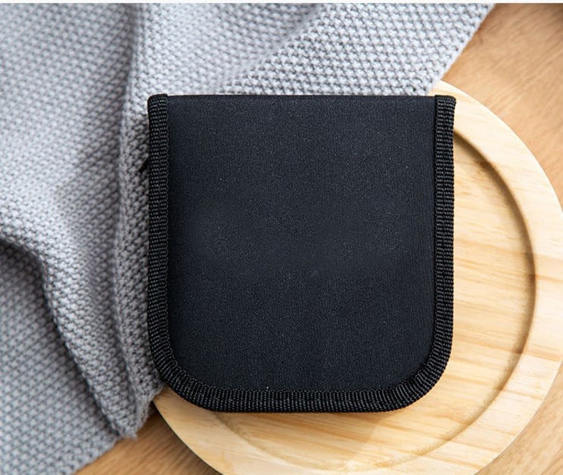May include: A black zippered pouch with a smooth, textured surface. The pouch is sitting on a wooden surface.