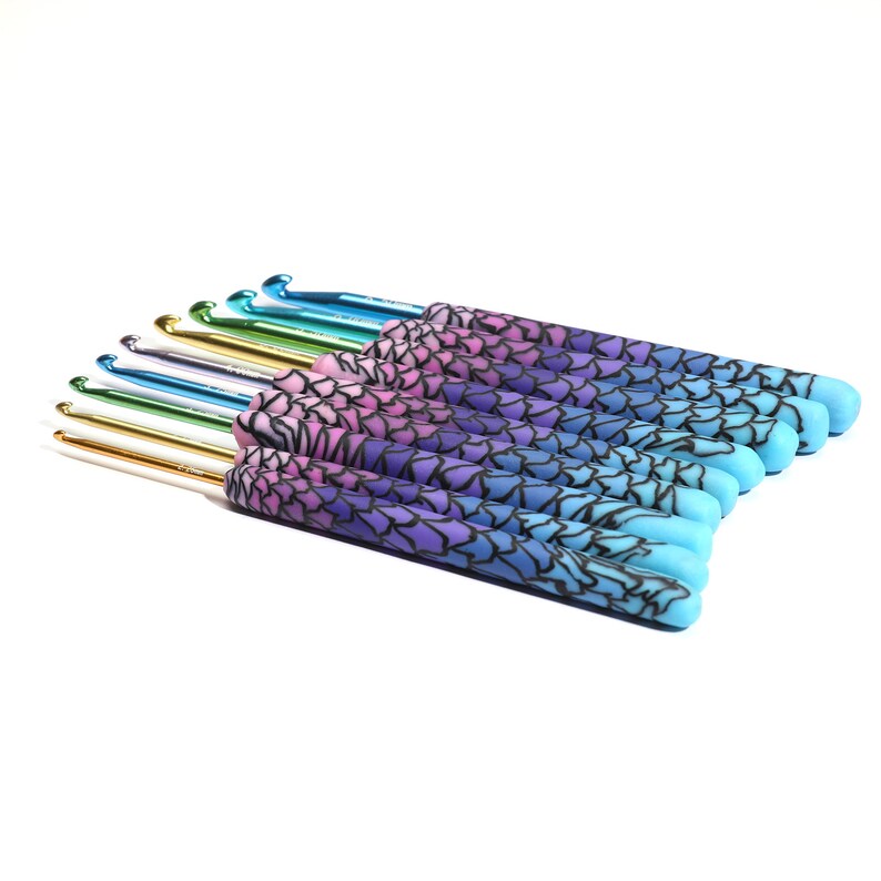 May include: A set of 12 crochet hooks with colorful, gradient-patterned handles. The handles are a mix of pink, purple, blue, and teal. The hooks are made of metal and have a shiny finish.