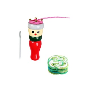 May include: A wooden spool knitter with a red base, green and cream midsection, and a pink top with gold beads. A gray needle and a stack of green and white knitted coasters are also shown.