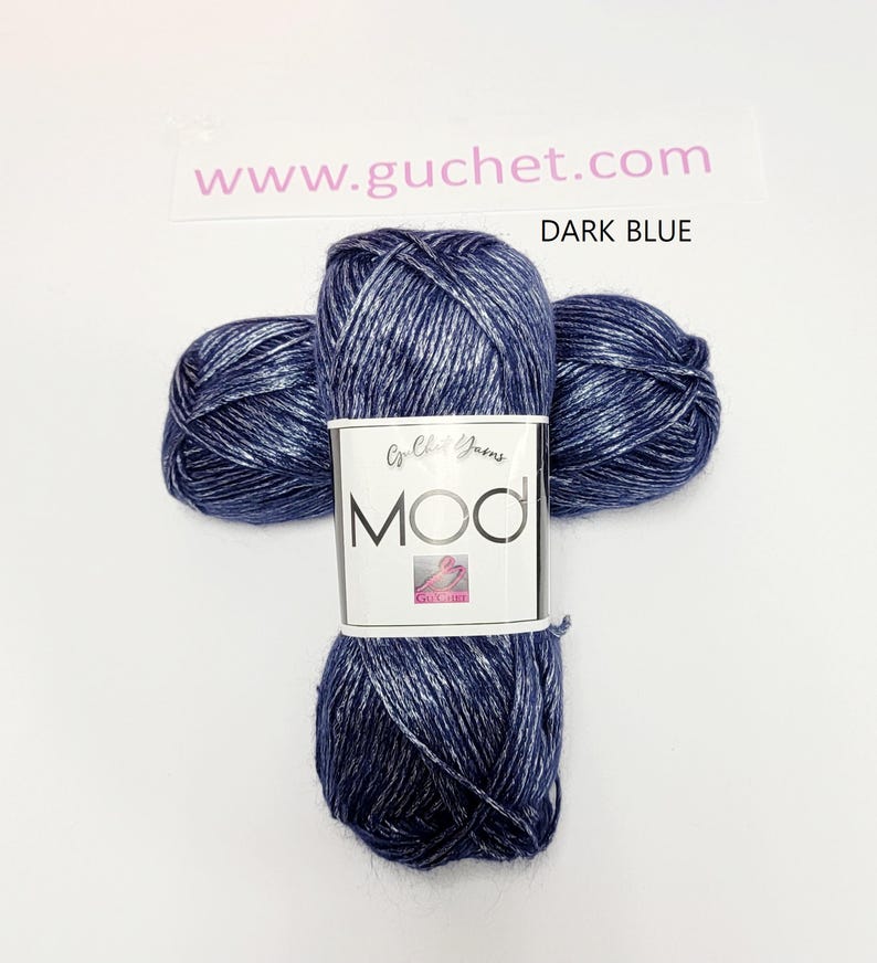 May include: Three skeins of dark blue yarn with a metallic silver sheen, arranged in a cross shape. A white paper label wraps around the center, featuring the text Crochet Yarns, MOD, and the website www.guchet.com, with the label text DARK BLUE.