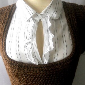 May include: A brown knitted sleeveless vest with a wide neckline. The vest is worn over a white collared shirt with black stripes.