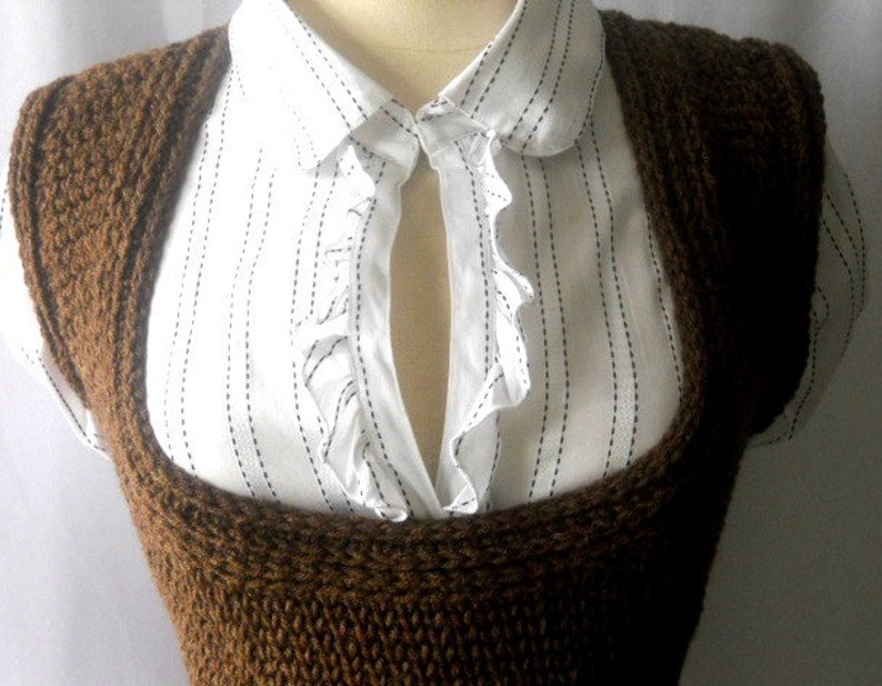 May include: A brown knitted sleeveless vest with a wide neckline. The vest is worn over a white collared shirt with black stripes.