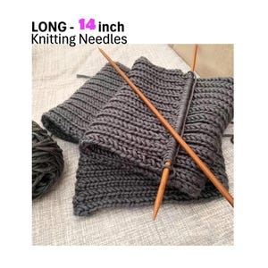 May include: A pair of 14 inch long knitting needles with a gray knitted scarf on them. The needles are made of wood and are brown in color. The scarf is made of a thick yarn and is a dark gray color.