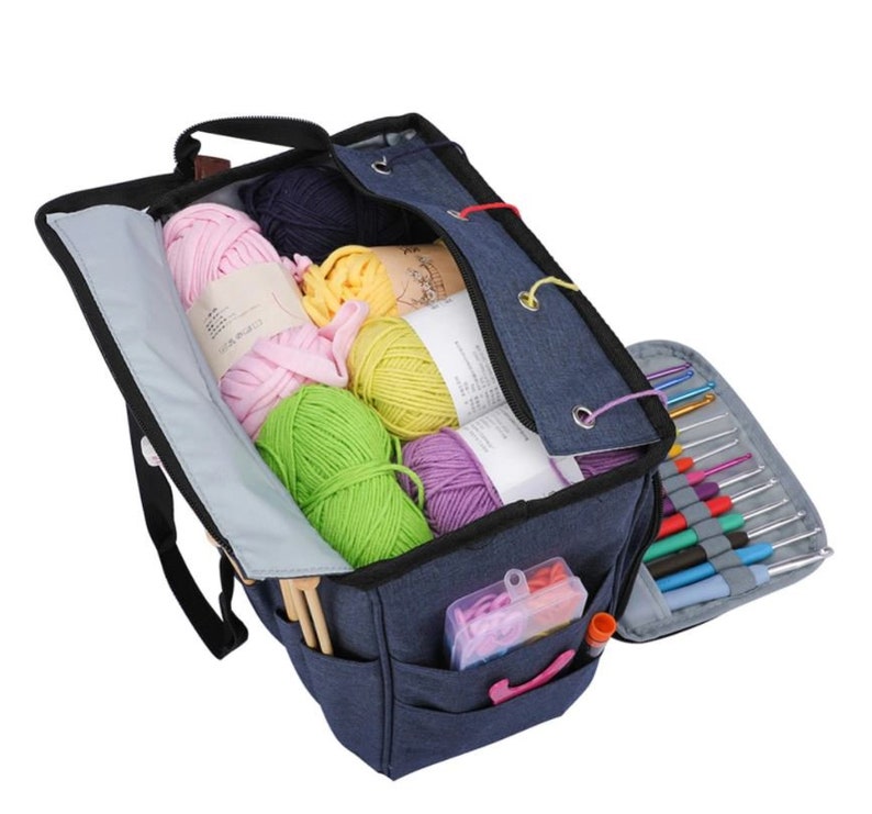 May include: A blue canvas knitting bag with multiple pockets and compartments. The bag is filled with colorful yarn balls and knitting needles.
