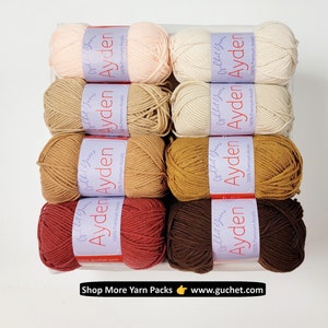 Op de afbeelding: Een verzameling garenbollen in verschillende kleuren, waaronder perzik, cr&egrave;me, beige en bruin. Elke bol heeft een label met "Ayden" en "100% Premium Acrylic". De tekst "Shop More Yarn Packs www.guchet.com" is ook zichtbaar.