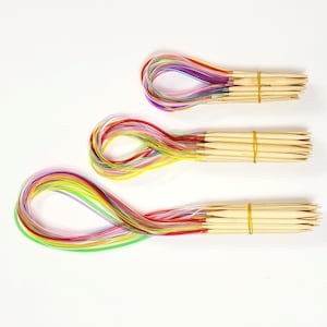 May include: Three sets of colorful circular knitting needles with wooden tips and rubber bands. The needles are arranged in a row from largest to smallest.