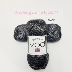 May include: Three skeins of black and silver metallic yarn arranged in a cluster. A white paper label wraps around the center skein, featuring the text Guchet Yarns, MOD, and a pink logo. The text www.guchet.com and the word BLACK are visible.