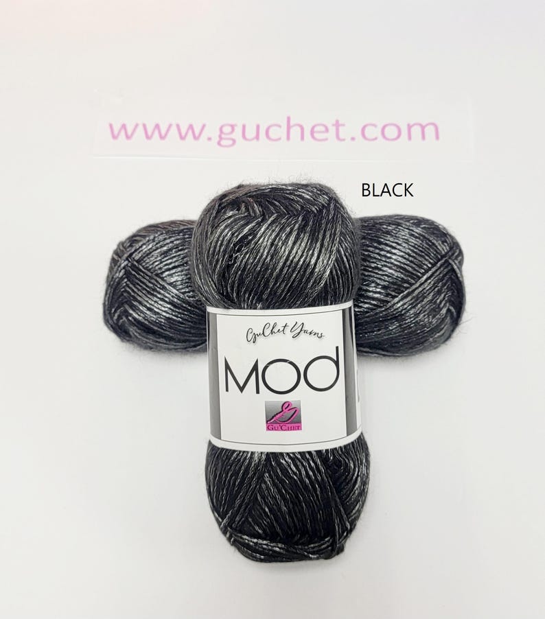 May include: Three skeins of black and silver metallic yarn arranged in a cluster. A white paper label wraps around the center skein, featuring the text Guchet Yarns, MOD, and a pink logo. The text www.guchet.com and the word BLACK are visible.