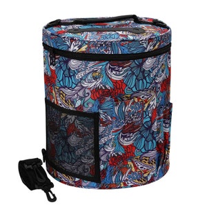 Puede incluir: Un bol de lana redondo con una cremallera negra y un estampado floral colorido. El bol tiene un bolsillo de malla en el lateral y una correa negra.