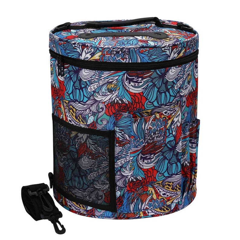 Puede incluir: Un bol de lana redondo con una cremallera negra y un estampado floral colorido. El bol tiene un bolsillo de malla en el lateral y una correa negra.
