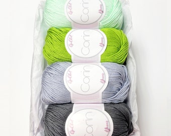 May include: Four skeins of yarn in different colors: light green, green, light gray, and gray. Each skein has a white label with the word "Corin" printed in pink.
