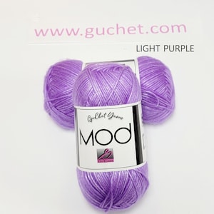 May include: Three balls of light purple yarn arranged in a cluster. Each ball features a white paper label with the text Guchet Yarns MOD and a small logo. The text www.guchet.com and the words LIGHT PURPLE are printed above the yarn balls.