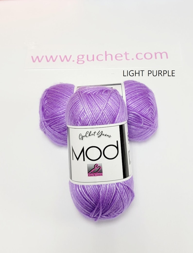 May include: Three balls of light purple yarn arranged in a cluster. Each ball features a white paper label with the text Guchet Yarns MOD and a small logo. The text www.guchet.com and the words LIGHT PURPLE are printed above the yarn balls.