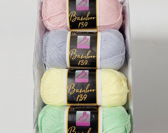 May include: Four skeins of yarn in a white basket. The yarn is in shades of pink, lavender, yellow, and green. Each skein has a black label with the text "Gu'Chet Bamboo 139" in white.