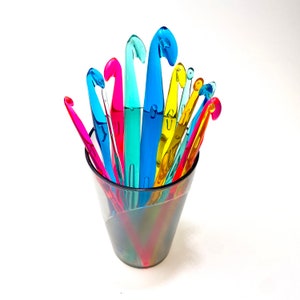 Pu&ograve; includere: Un barattolo di vetro trasparente pieno di una variet&agrave; di uncinetti di plastica colorati. Gli uncinetti sono disposti a ventaglio, con le punte rivolte verso l'alto.