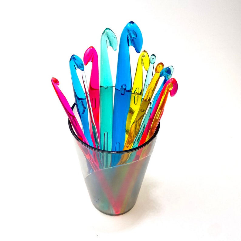 Pu&ograve; includere: Un barattolo di vetro trasparente pieno di una variet&agrave; di uncinetti di plastica colorati. Gli uncinetti sono disposti a ventaglio, con le punte rivolte verso l'alto.