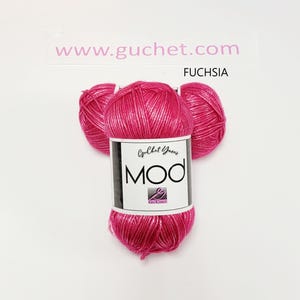 May include: A skein of fuchsia yarn with a metallic sheen, featuring a white paper label that reads Guchet Yarns MOD and includes a small logo. The text www.guchet.com and the word FUCHSIA are printed above the yarn on a white background.