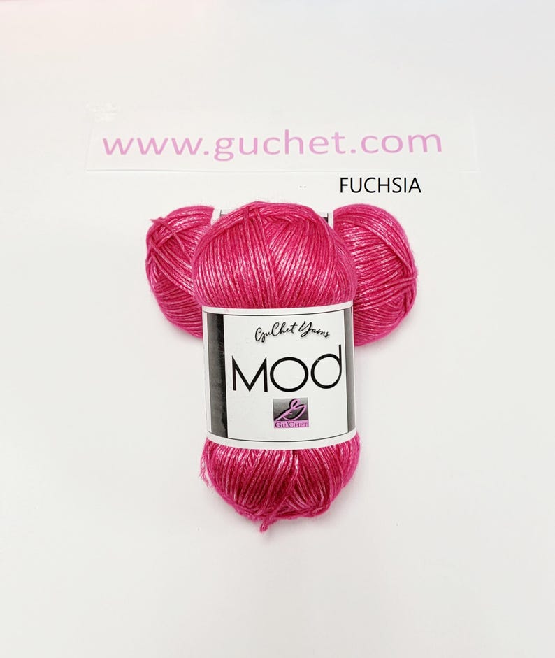 May include: A skein of fuchsia yarn with a metallic sheen, featuring a white paper label that reads Guchet Yarns MOD and includes a small logo. The text www.guchet.com and the word FUCHSIA are printed above the yarn on a white background.