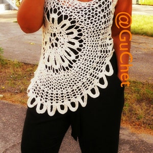 May include: A woman wearing a white crocheted top with a black and white floral design. She is also wearing black pants and leopard print shoes.