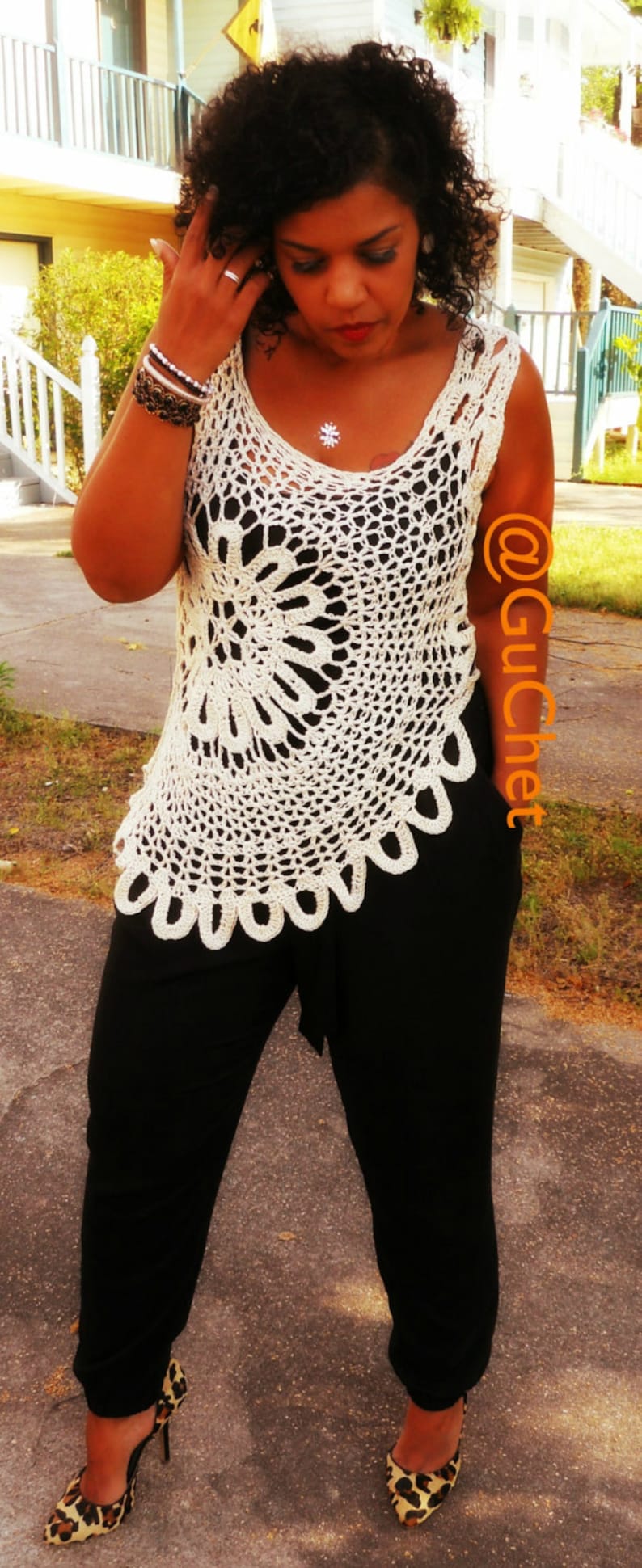 May include: A woman wearing a white crocheted top with a black and white floral design. She is also wearing black pants and leopard print shoes.