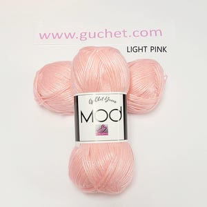 May include: Three skeins of light pink yarn arranged together. A white paper label wraps around the center, featuring the text "www.guchet.com", "LIGHT PINK", "Cy Chet Yarns", and "MOD" in bold black letters with a small pink logo icon.
