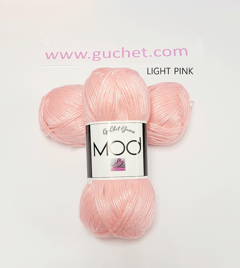 May include: Three skeins of light pink yarn arranged together. A white paper label wraps around the center, featuring the text "www.guchet.com", "LIGHT PINK", "Cy Chet Yarns", and "MOD" in bold black letters with a small pink logo icon.