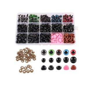May include: A clear plastic storage box filled with various sizes and colors of plastic safety eyes for crafts. The box has 12 compartments, each filled with a different color or size of eyes. There are also loose safety eyes and washers in the image.