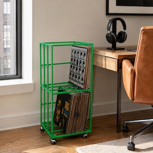 May include: A bright green metal storage rack with two open shelves on four small wheels. The rack is filled with vinyl records, including one titled A Hard Day's Night and another titled Count Basie, organized vertically within the frame.
