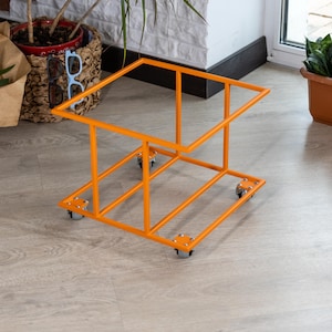 Op de afbeelding: Een oranje metalen plantenstandaard met een rechthoekig frame en vier kleine wielen. De standaard heeft een ontwerp met twee niveaus, met een boven- en onderframe verbonden door verticale steunen. De standaard is ontworpen om planten te bevatten.