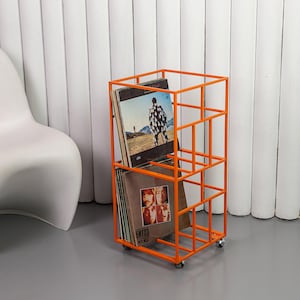 May include: An orange metal record storage rack on wheels. The rack is filled with vinyl records. The rack has a rectangular shape with a grid-like design. The records have album art visible.