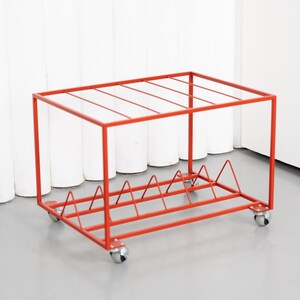 May include: A red metal storage rack on wheels. The rack has a rectangular frame with a series of horizontal bars on top and a triangular design at the bottom. The rack is designed to hold items and has four small wheels.