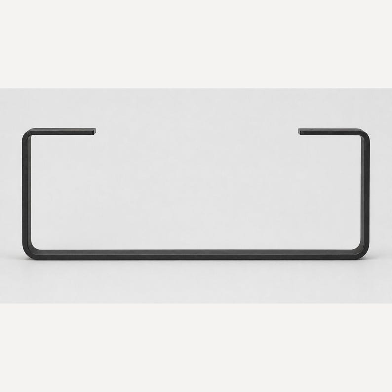 May include: A matte black metal bracket featuring a wide, rectangular U-shape design with two short, inward-facing horizontal arms at the top. The structure is composed of a single continuous piece of flat, uniform metal with rounded corners.