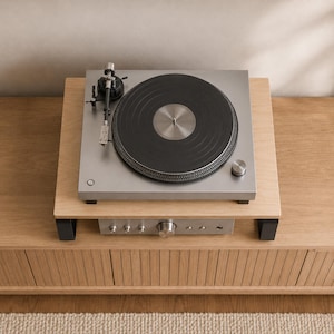 May include: A silver turntable with a black platter and a black tonearm sits on a light wood platform. Below the platform, a silver audio amplifier with multiple circular control knobs and a headphone jack is visible on the wooden surface.