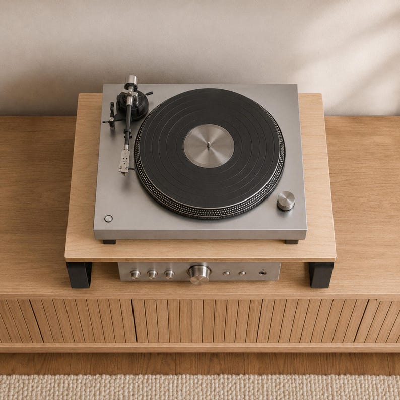 May include: A silver turntable with a black platter and a black tonearm sits on a light wood platform. Below the platform, a silver audio amplifier with multiple circular control knobs and a headphone jack is visible on the wooden surface.