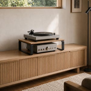 May include: A light wood media console with vertical slat cabinet doors. On top sits a two-tier wooden shelf with black metal legs, holding a grey turntable on the top level and a silver audio amplifier with multiple control knobs below.