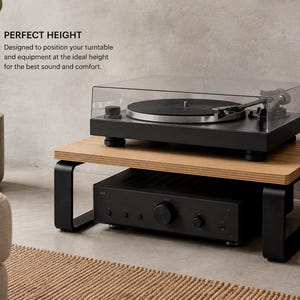 May include: A wooden turntable stand with black metal legs, featuring a light wood top surface and a black base. The stand holds a black turntable with a clear cover on top and a black audio amplifier underneath. Text reads: PERFECT HEIGHT.