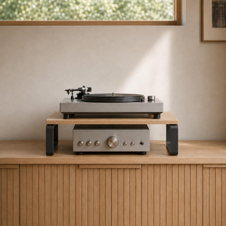 May include: A light gray turntable sits atop a wooden monitor stand with black metal legs. Beneath the stand is a matching light gray audio amplifier featuring several circular control knobs and a headphone jack on its front panel.