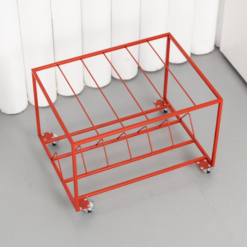 May include: A red metal storage rack with a rectangular frame and angled dividers. The rack sits on four small caster wheels. The design is simple and modern, suitable for organizing items.